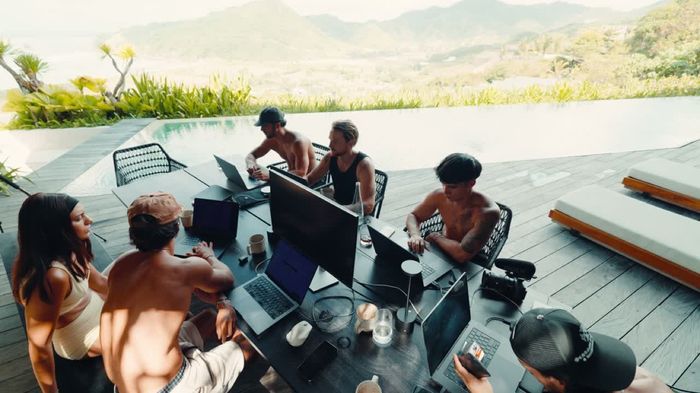The team working at a long table outdoors, pool and mountains behind.